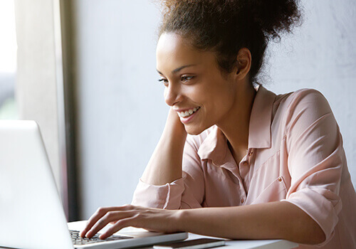 Woman Smiling and Typing on Her Laptop Computer